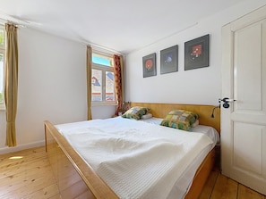 A bedroom with a wooden bed, a window with curtains, and three framed pictures on the wall.