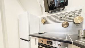Una cuina compacta amb forn integrat, fogó d'acer inoxidable i prestatge penjat per a gots.