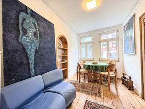A room with a blue sofa, a table with chairs, a bookshelf, and a large abstract painting on the wall.