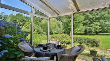 Une véranda avec une table dressée pour le repas, des meubles en osier et une vue sur un jardin luxuriant.