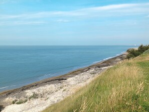 Eine Küstenlandschaft mit felsiger Küste, grünen Wiesen und freiem Blick auf das Meer.