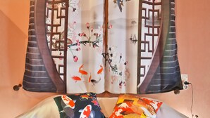 A room with a bed, two pillows with floral designs, and a curtain with a traditional pattern.