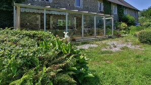 A stone building with a conservatory featuring glass walls and a garden with various plants.