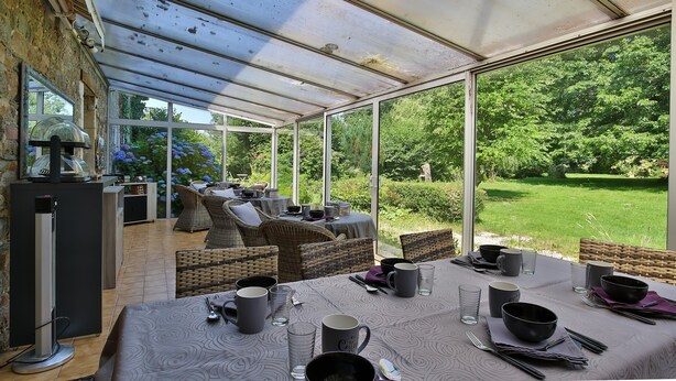 A covered outdoor dining area with wicker furniture, a table set for four, and a view of a lush garden.