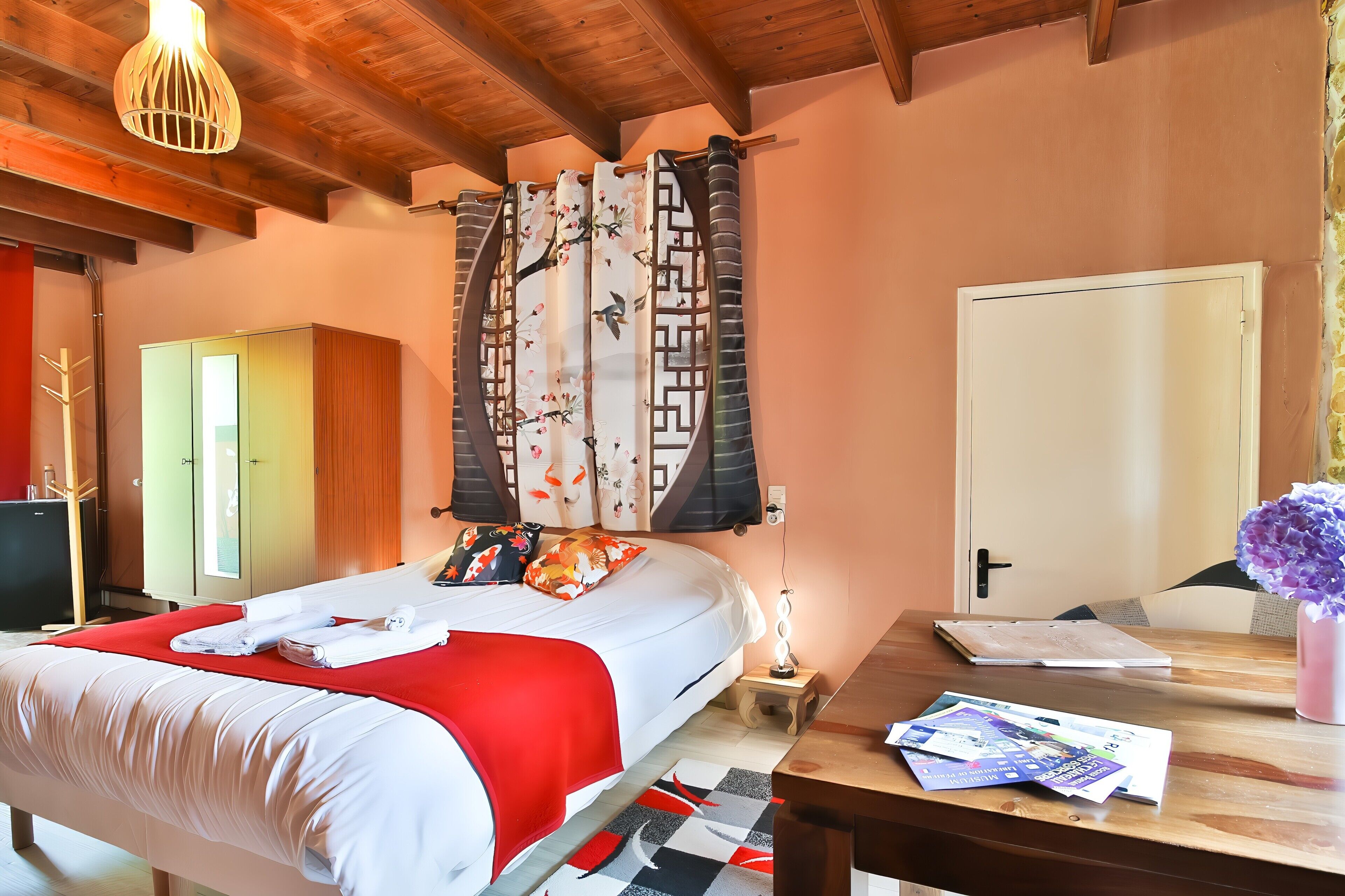 A hotel room with a bed, a desk, a lamp, and a door.