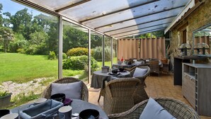 An outdoor patio with wicker furniture, a glass enclosure, and a view of a garden.