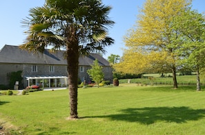 A large stone house with a covered patio, a lawn, and a palm tree. - Le Pigeonnier – Charming Accommodation with Private Terrace (Saint-Sauveur-Villages)