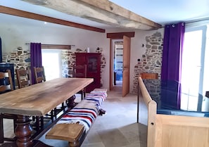 A rustic dining area with a wooden table and benches, stone walls, and a glass railing overlooking a balcony. - Le Pigeonnier – Charming Accommodation with Private Terrace (Saint-Sauveur-Villages)