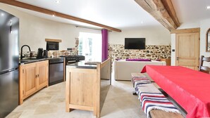 A compact kitchen with modern appliances, a stone wall, and a cozy living area with a bed and a TV.