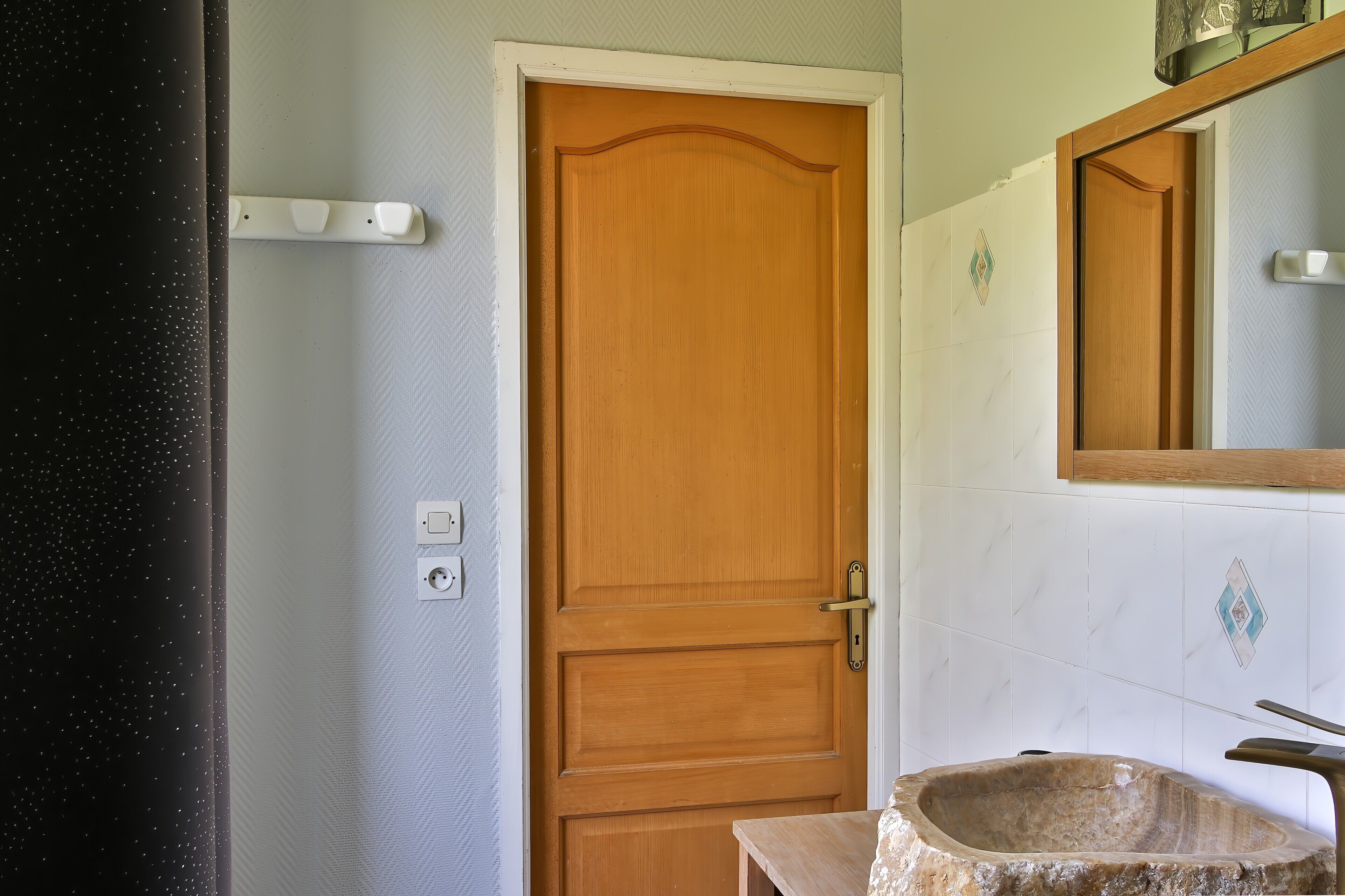 Een badkamer met een houten deur, een wastafel met een stenen kom, en een spiegel boven de wastafel.