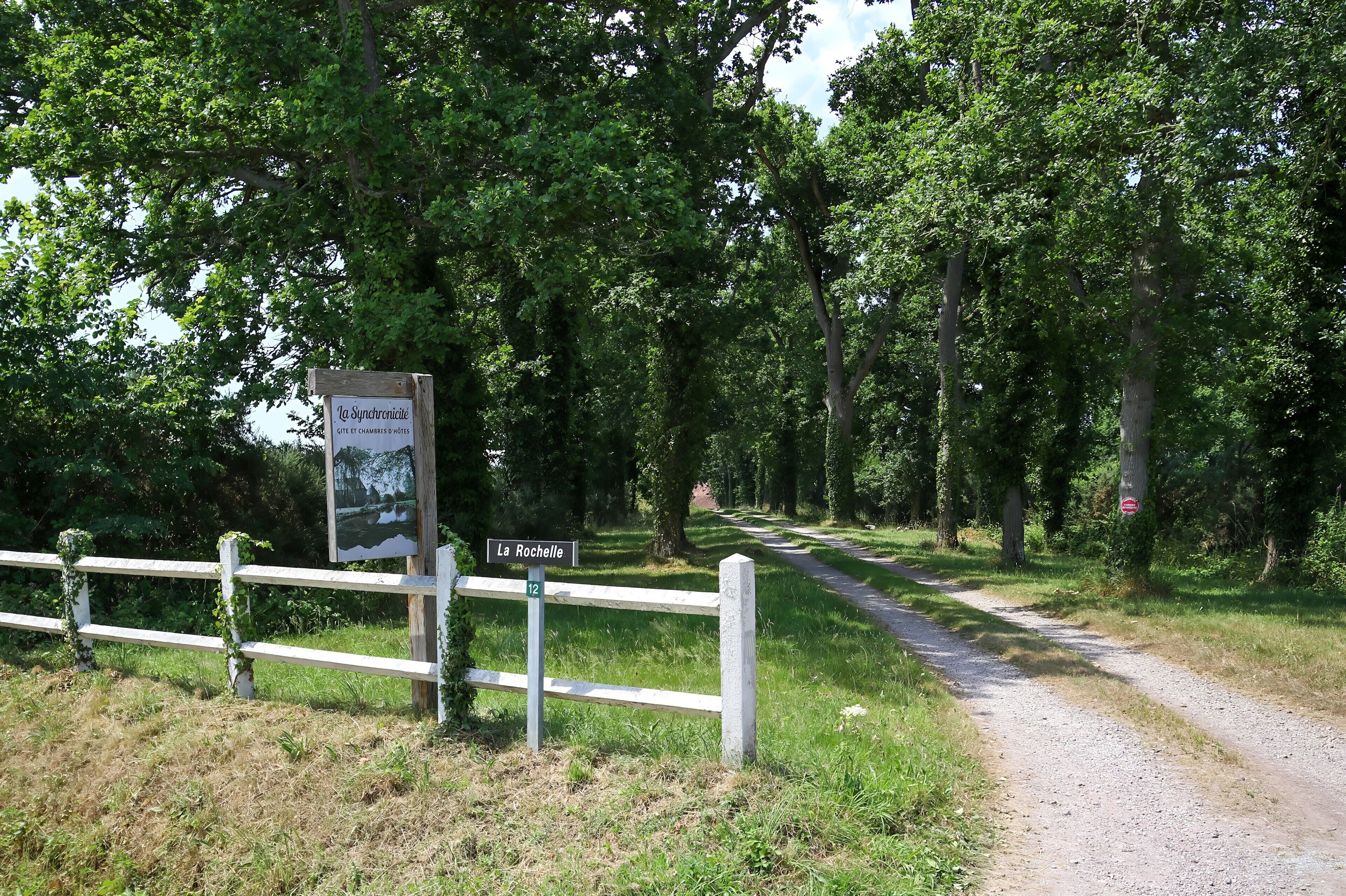 Une route de campagne bordée d’une clôture en bois et d’un panneau indiquant « La Rochelle » et « Gîte et chambres d’hôtes ».