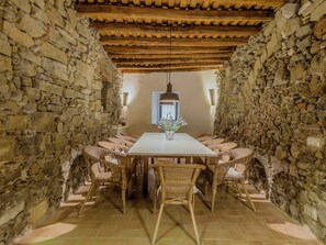 A stone-walled dining area with a wooden ceiling, a central table, wicker chairs, and a hanging light fixture. - Mas Silvestre by Interhome (La Bisbal D'Emporda)