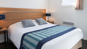 Une chambre d’hôtel comprenant un lit, deux tables de chevet, une fenêtre avec des rideaux et un climatiseur fixé au mur.