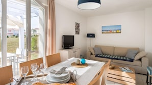 Une pièce comprenant une table à manger dressée pour deux personnes, un canapé, un téléviseur et une vue sur l’extérieur.