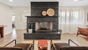 A living room with a stone fireplace, two woven wall decorations, a potted plant, and a wooden table with chairs. - The Hideaway at Chandler (Chandler)