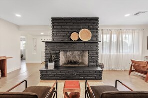A living room with a stone fireplace, two woven wall decorations, a potted plant, and a wooden table with chairs. - The Hideaway at Chandler (Chandler)