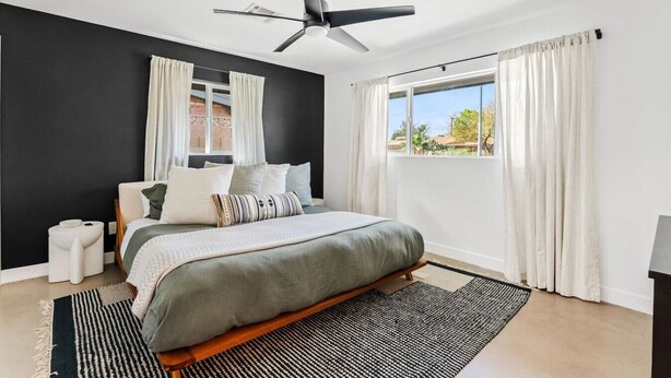 A modern bedroom with a bed, a ceiling fan, a window with curtains, and a view of the outdoors. - The Hideaway at Chandler (Chandler)