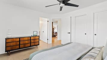 A bedroom with a bed, a dresser, a ceiling fan, and a door leading to another room.