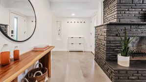 A modern interior with a wooden console table, a mirror, a stone fireplace, and a white storage unit. - The Hideaway at Chandler (Chandler)