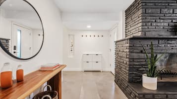 A modern interior with a wooden console table, a mirror, a stone fireplace, and a white storage unit.