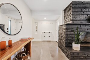 A modern interior with a wooden console table, a mirror, a stone fireplace, and a white storage unit. - The Hideaway at Chandler (Chandler)
