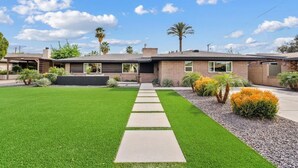 A modern two-story house with a well-maintained lawn, a paved driveway, and a variety of landscaping including palm trees and shrubs. - The Hideaway at Chandler (Chandler)