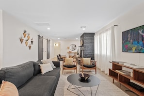 Ein modernes Wohnzimmer mit einer Couch, Sesseln, einem Couchtisch, einem Kamin und einem Bild an der Wand.