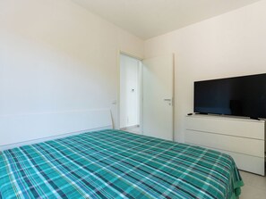 Ein Schlafzimmer mit einem Bett, einem Fernseher auf einer Kommode und einer Tür zu einem anderen Raum.