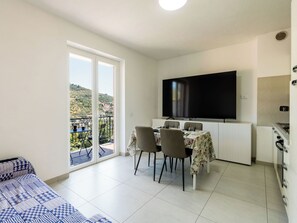 Ein modernes Wohnzimmer mit Balkon, einem Essbereich mit vier Stühlen, einem flachbildfernseher an der Wand und einer Küche mit Herd.