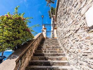 Eine steinerne Treppe führt zu einem Gebäude mit einem blauen Tor, umgeben von viel Grün und blauem Himmel.