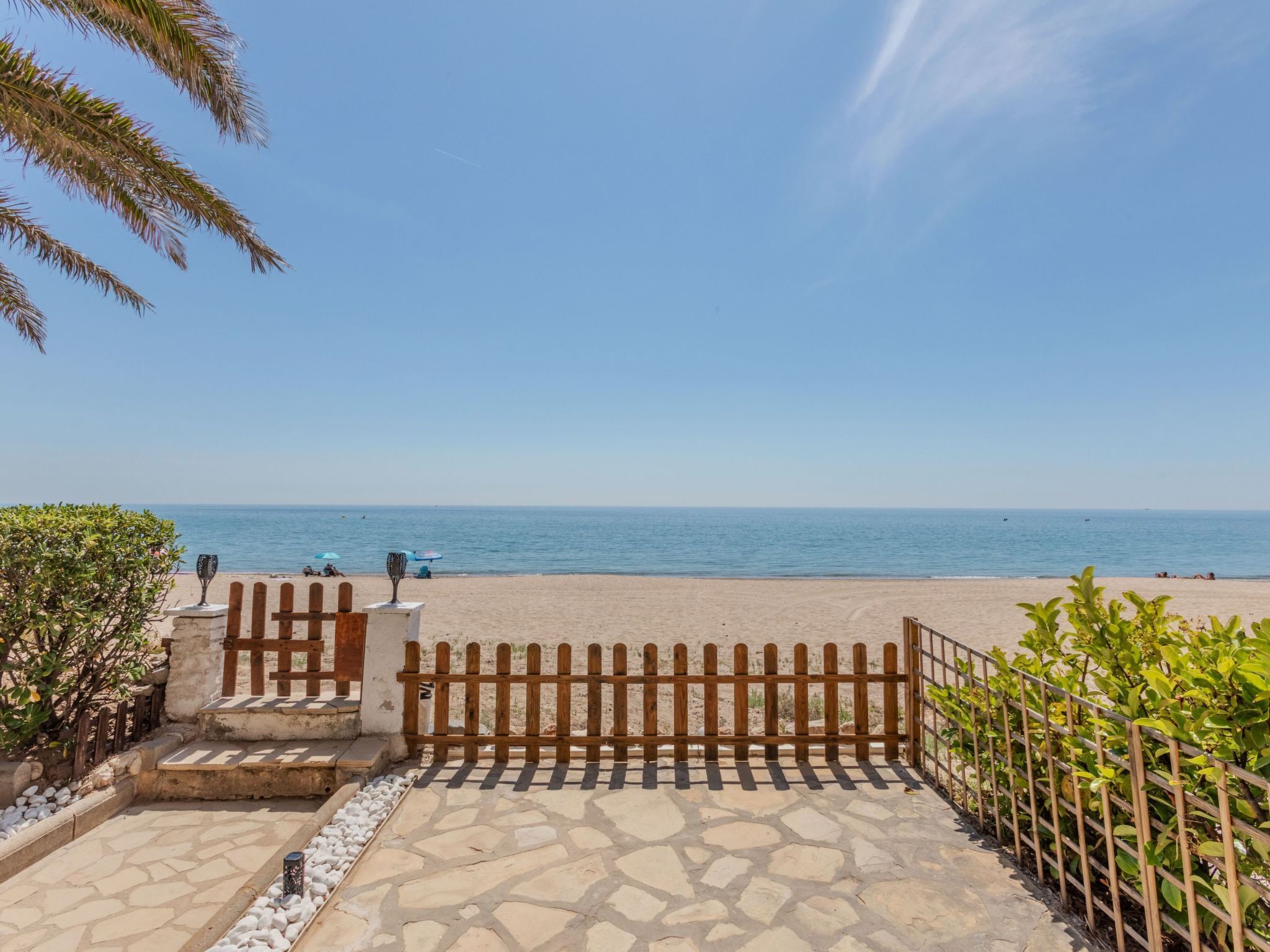 A beach view with a wooden fence, a stone pathway, and a clear sky.
