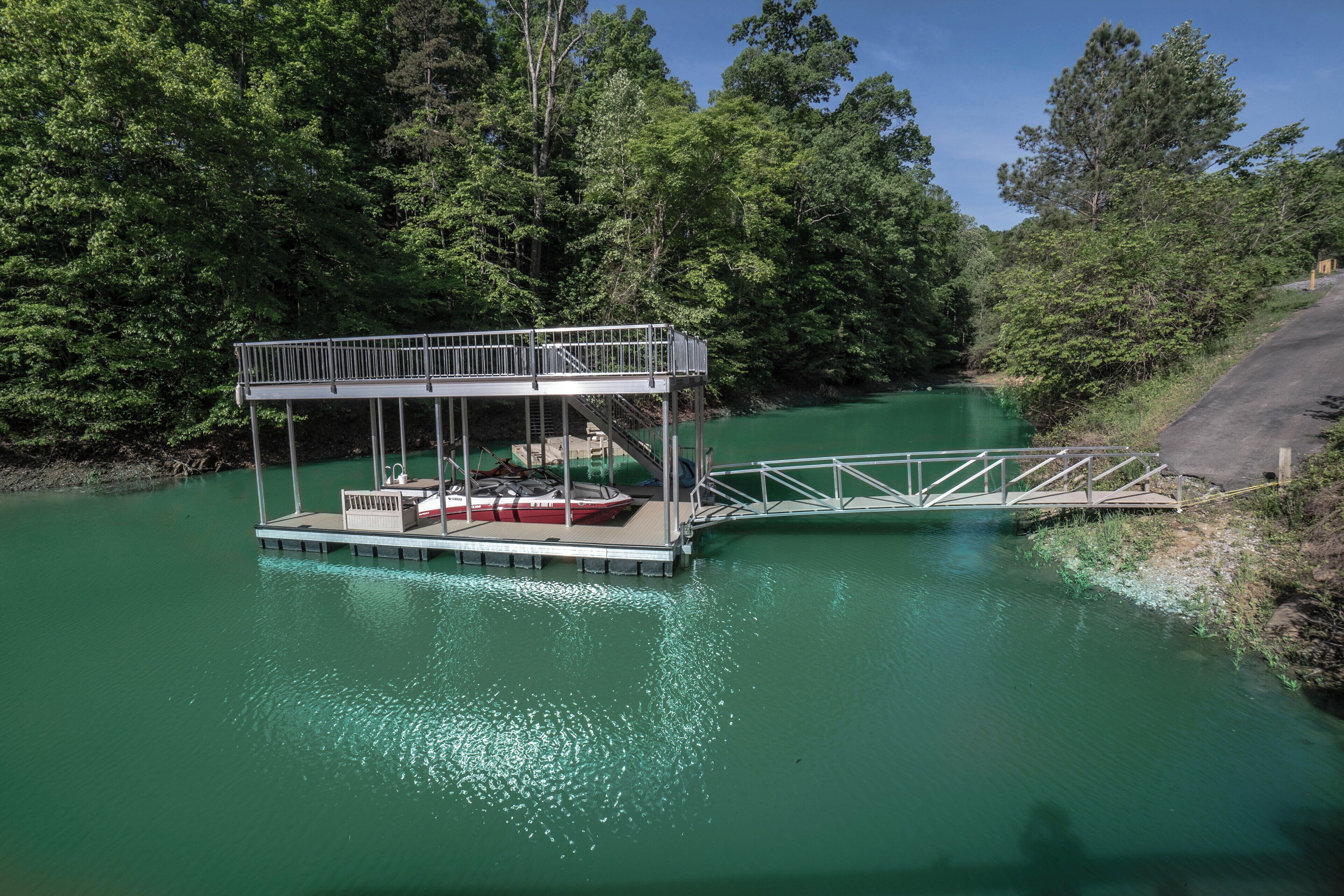 A dock with a covered seating area and a small boat, surrounded by dense forest and a calm green river.