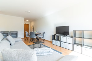 Ein modernes Wohnzimmer mit einer Couch, einem Esstisch mit Stühlen, einem Fernseher und eingelassenen Stauraumelementen.
