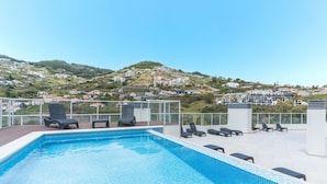 En pool på taket med solstolar och utsikt över en stad som ligger på en sluttning.