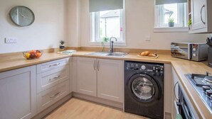 A compact kitchen with a washing machine, a sink, and a toaster. - Mitchell Apartment - 1 Bedroom (North Lanarkshire)