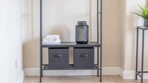 A corner with a metal shelf unit, two drawers, a folded towel, and a decorative vase. - Mitchell Apartment - 1 Bedroom (North Lanarkshire)