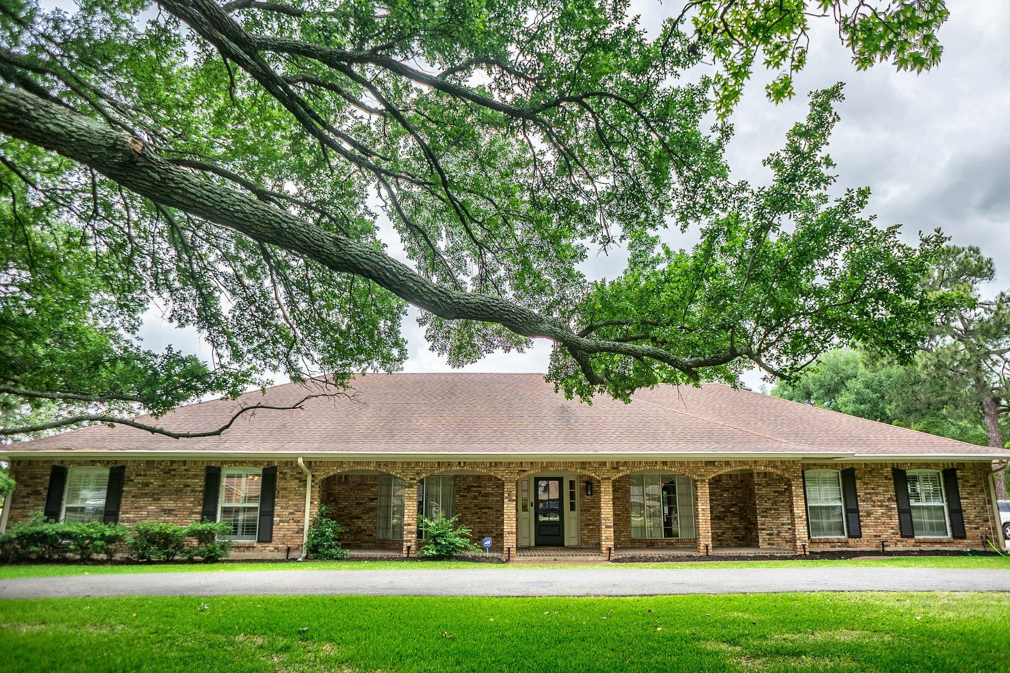 A two-story brick house with a front porch, a garage, and a large tree in front.