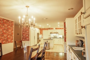 A kitchen with white cabinets, a chandelier, and a dining area with a table and chairs.