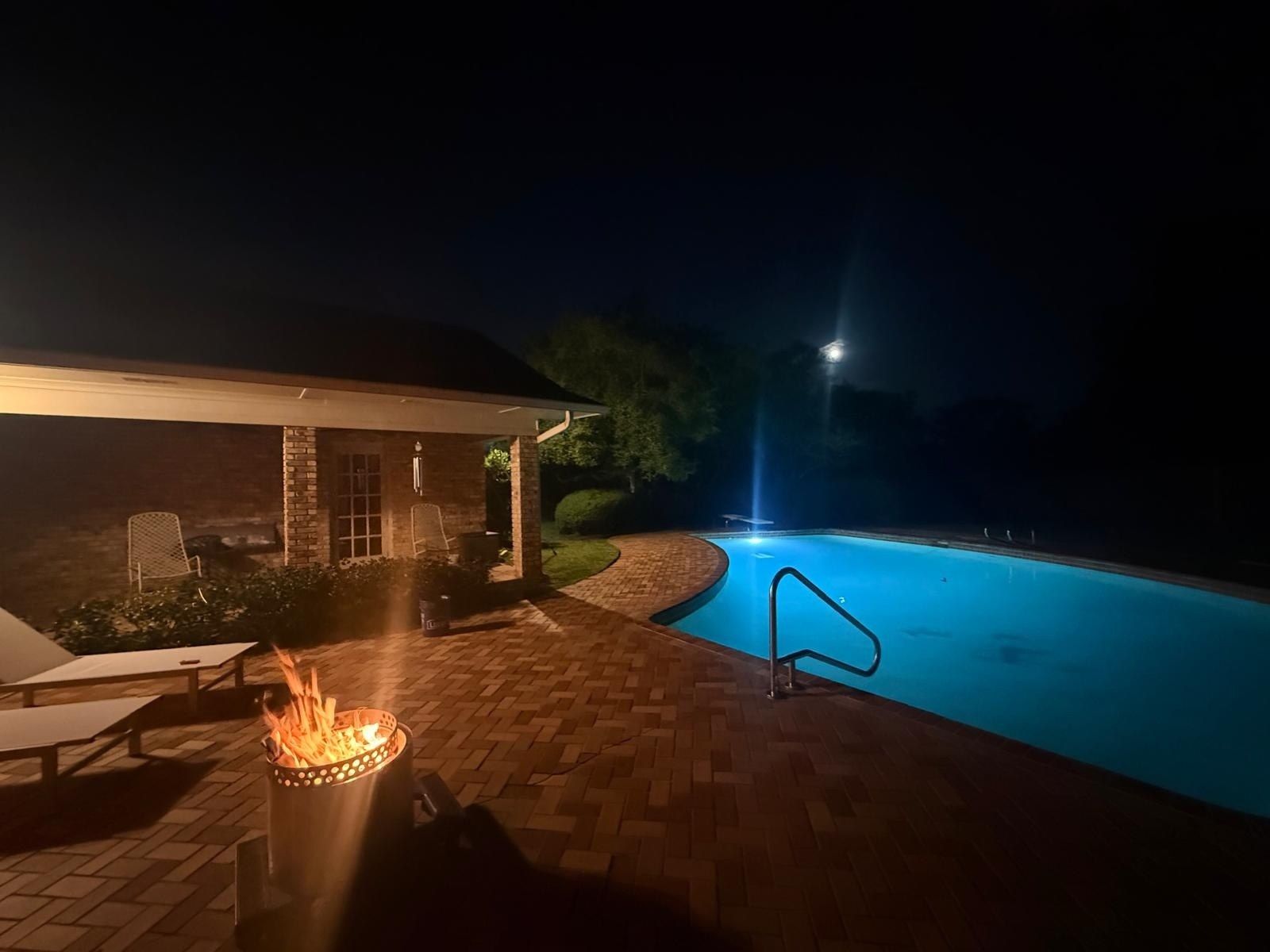 A swimming pool with a fire pit and lounge chairs.