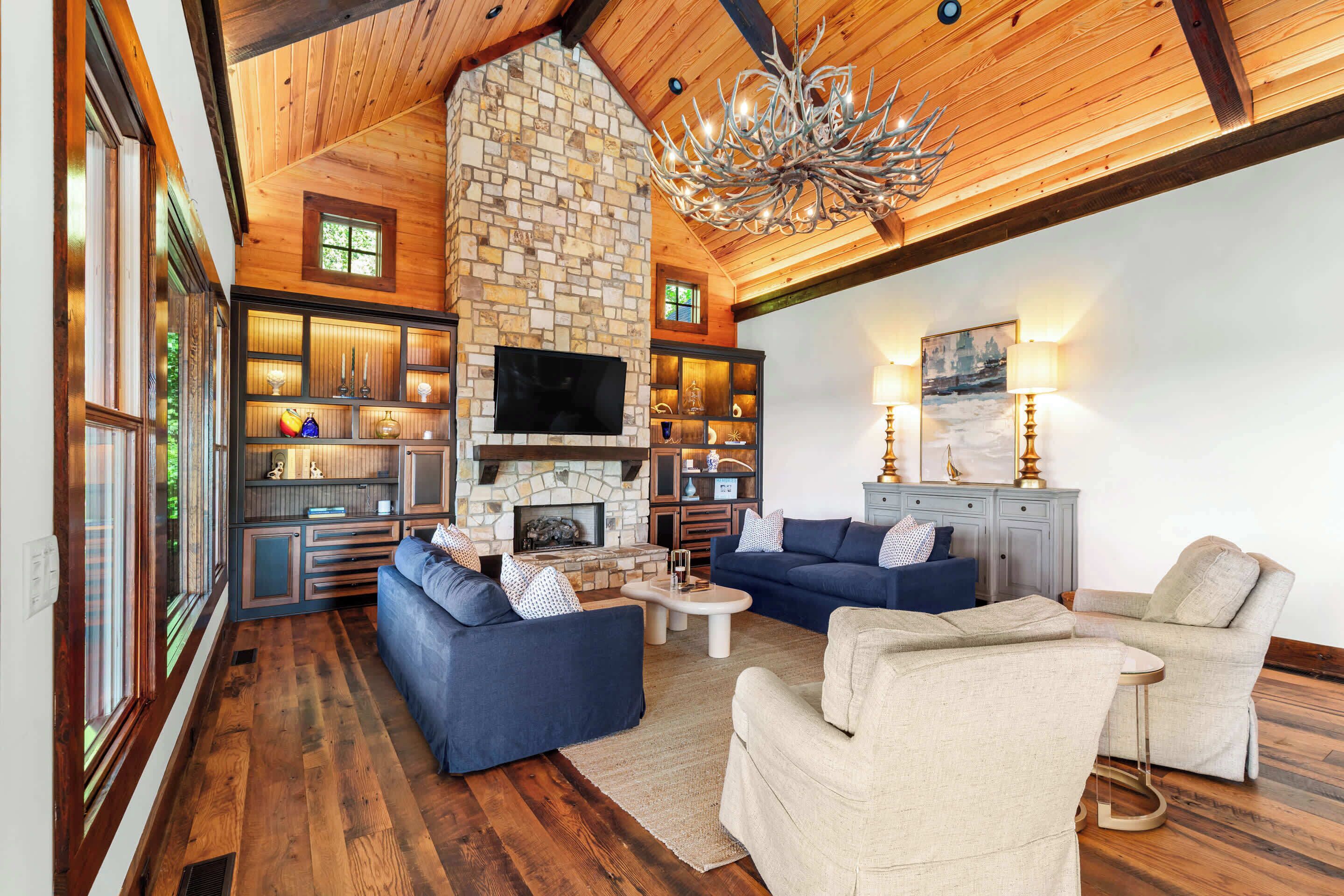 Un salón espacioso con chimenea de piedra, techo de madera y televisor.