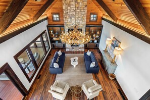A spacious loft-style living area with a stone fireplace, dark blue sofas, and a chandelier. - Stunning Big Water Views - Pet-friendly, Game Room (Sparta)
