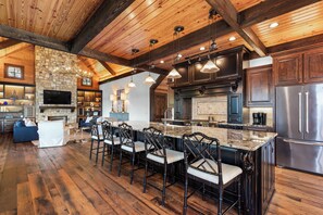 A spacious kitchen with a stone fireplace, wooden beams, and a large island with bar stools. - Stunning Big Water Views - Pet-friendly, Game Room (Sparta)