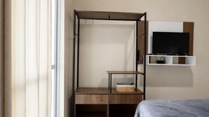 A bedroom with a bed, a TV on the wall, a wooden desk, and a window with curtains. - Casa Maré | 250m from Mariscal beach (Bombinhas)