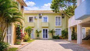 A yellow building with a paved courtyard, air conditioning units, and potted plants. - Casa Maré | 250m from Mariscal beach (Bombinhas)