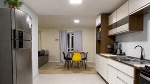 A modern kitchen with a refrigerator, stove, and dining area with a table and chairs. - Casa Maré | 250m from Mariscal beach (Bombinhas)