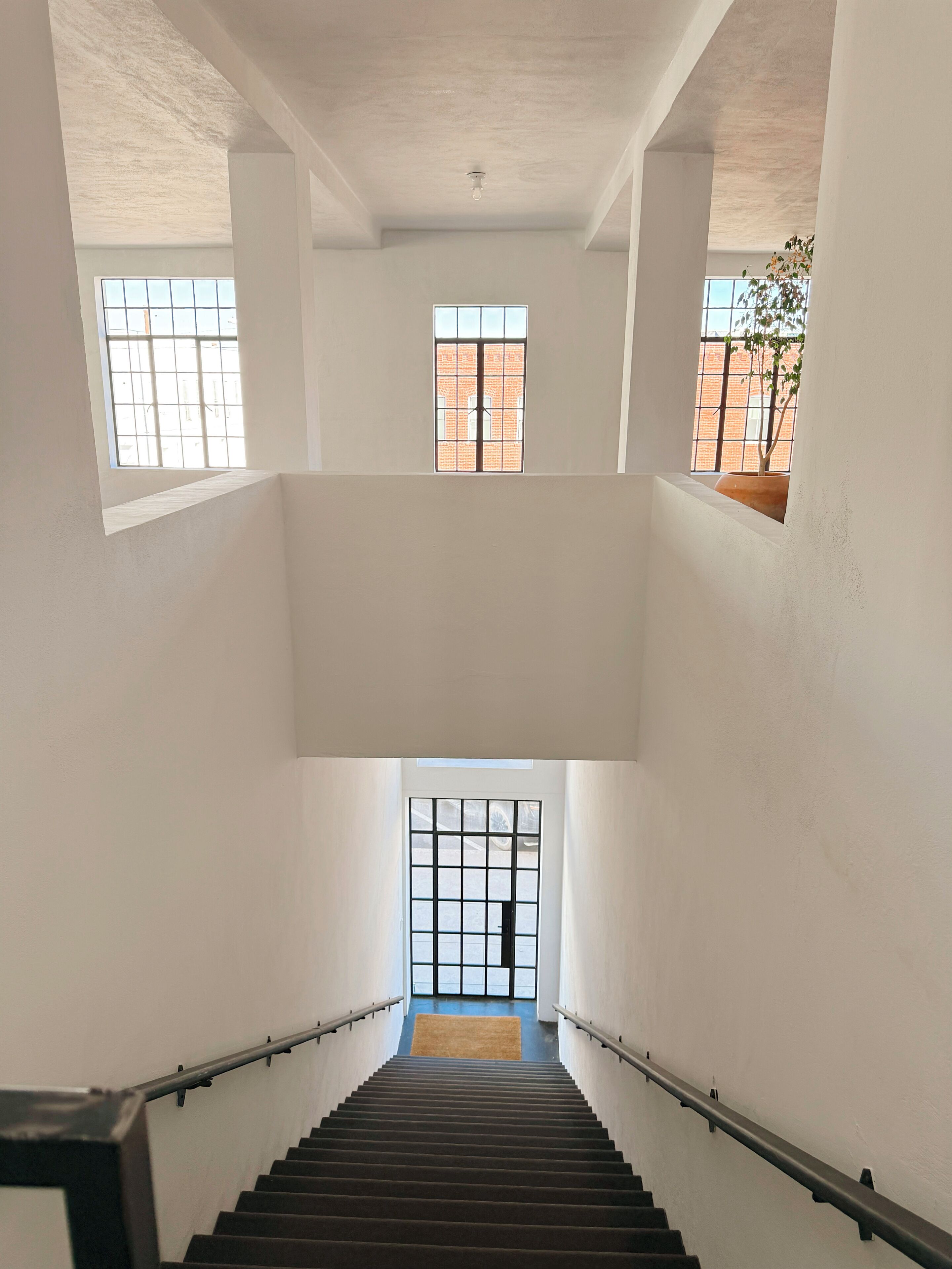 Un intérieur à plusieurs niveaux, doté d’un escalier central, de murs blancs et de grandes fenêtres.