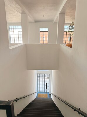Ein mehrgeschossiges Interieur mit einer zentralen Treppe, weißen Wänden und großen Fenstern.