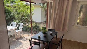 Una stanza con pavimento in legno, un tavolo con sedie, una finestra con tende e vista su un giardino.