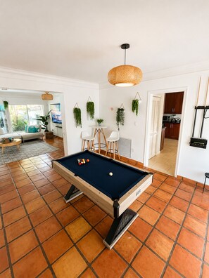 A pool table in a room with a tiled floor, a hanging plant, and a view into a kitchen area. - Miami World Cup Pool House Near Hard Rock Stadium • 5 Min to Beach (Hollywood)