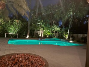 Piscina rodeada de palmeras y una valla de madera de noche.